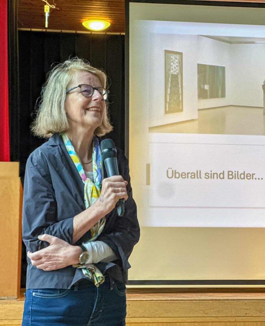 Dozentin mit Mikrofon bei einem Vortrag vor einer Präsentation im Hintergrund.